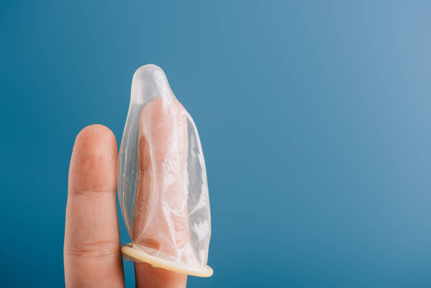 abgeschnittene Ansicht von Fingern mit Kondom auf blauem Grund, Verhütungskonzept - Foto, Bild