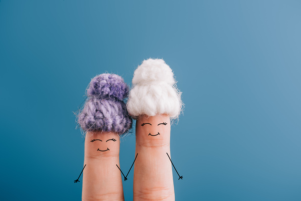 cropped view of fingers as friends in knitted hats holding hands isolated on blue - Zdjęcie, obraz