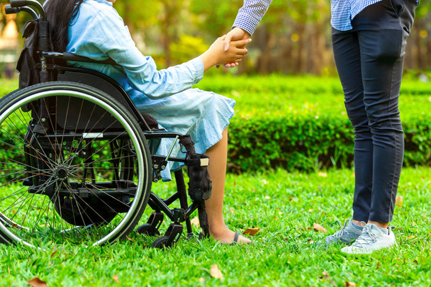 Νεαρή γυναίκα σε αναπηρική καρέκλα, κρατώντας τα χέρια με τον επιστάτη άνθρωπο σε pu - Φωτογραφία, εικόνα