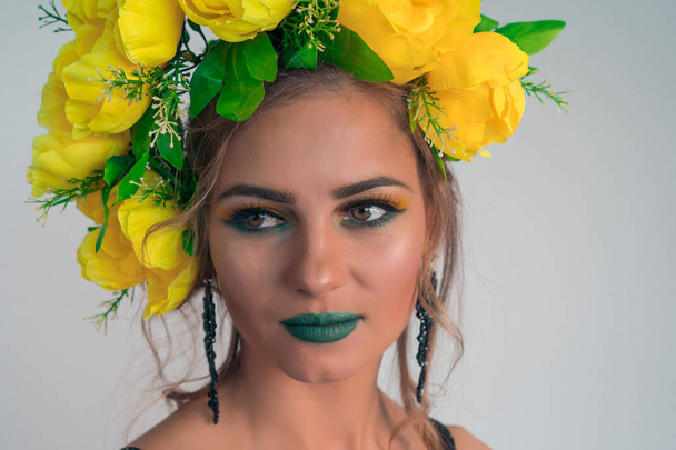 Close-up face of a beautiful girl with bright makeup and large yellow flowers on her head - Foto, Bild