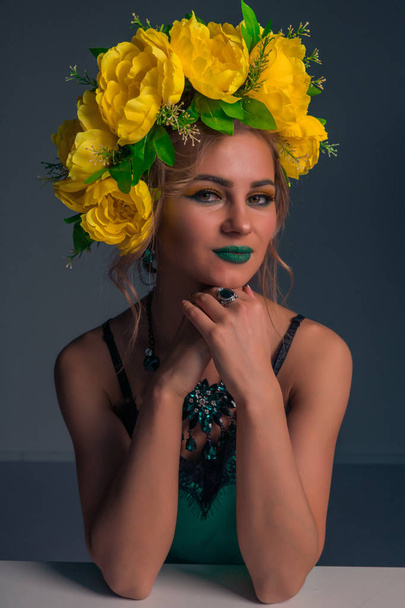 Portrait of a cute beautiful blonde with a rim of yellow flowers and bright makeup on a dark background - Foto, Imagem