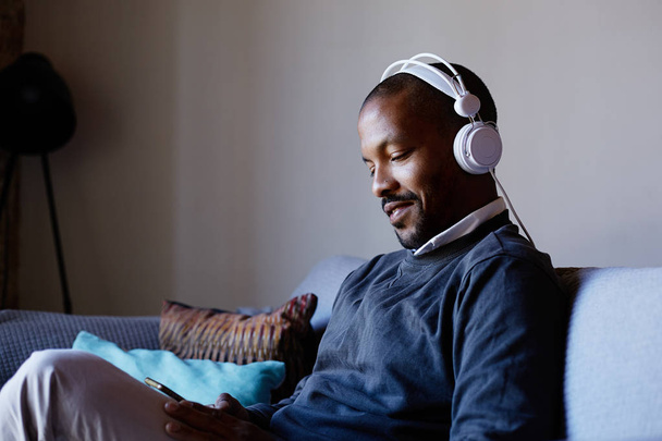 Attractive African American man with headphones listening to music on his phone. Concept of relaxation. - Zdjęcie, obraz
