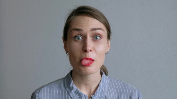 A Beautiful Girl Fools Around And Shows Her Tongue on Background of White Wall. - Video