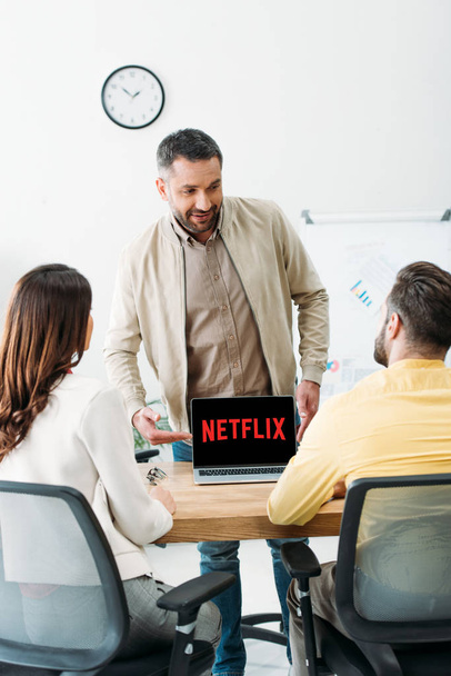 advisor pointing with hand at laptop with netflix website on screen to man and woman in office - Φωτογραφία, εικόνα