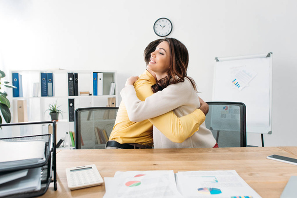 man and woman sitting at table with documents and hugging in office - Photo, Image