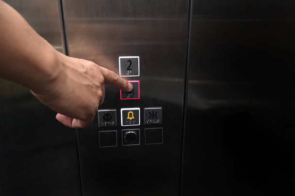 Męska dłoń po naciśnięciu przyciski sterowania wnętrza winda ma panelu Braille'a dla niepełnosprawnych i puste miejsca na tekst. - Zdjęcie, obraz