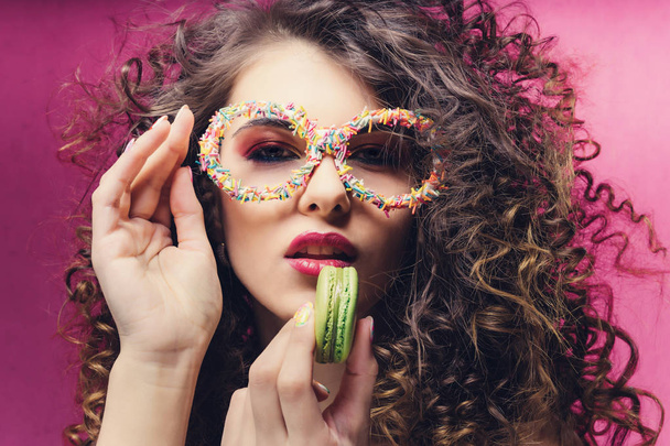Beautiful girl eat green macaroon in confectionery dressing glasses - Фото, изображение