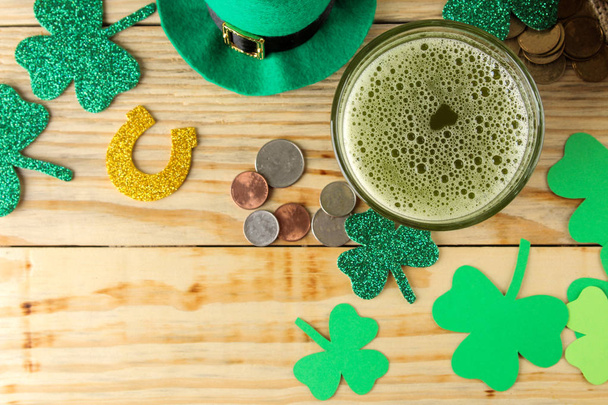 聖パトリックの日。お祝い。緑のレプラコーンの帽子と緑のビール、蝶ネクタイ、コイン、天然木製の背景にクローバー。トップ ビュー - 写真・画像