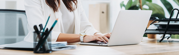 vista ritagliata di donna d'affari seduta a tavola con computer portatile e digitando in ufficio
 - Foto, immagini