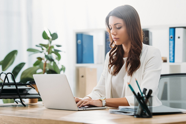 attraente donna d'affari seduta a tavola con computer portatile e digitando in ufficio
 - Foto, immagini
