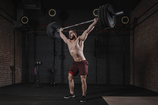 Cross fit athlete lifting barbell overhead at the gym. Shirtless man doing functional training. Practicing powerlifting. - Photo, Image