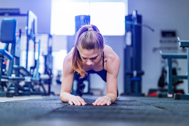 Gorgeous blonde woman warming up and doing some push ups a the gym. Young woman with muscular body. Fitness concept. - Foto, afbeelding