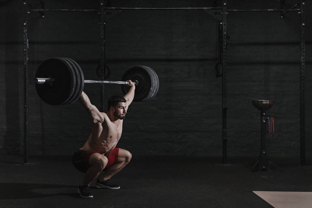 Young crossfit athlete lifting barbell overhead at the gym. Copy space - Foto, Imagem