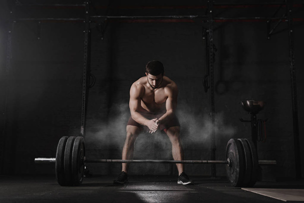 Crossfit athlete clapping hands and preparing for weight lifting at the gym. Barbell magnesia protection dust cloud. Handsome man doing functional training. Practicing powerlifting. Workout exercises. - Photo, Image