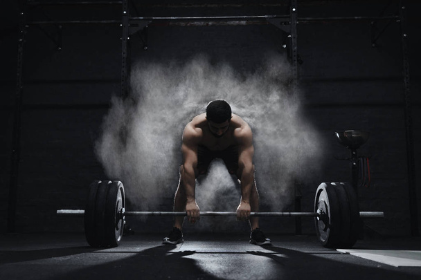 Crossfit athlete preparing to lift heavy barbell in a cloud of dust at the gym. Barbell magnesia protection. - Photo, Image