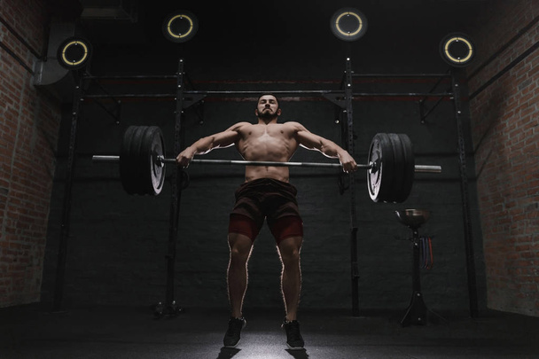 Joven atleta crossfit levantando pesadas barras en el gimnasio. Practicando levantamiento de pesas
. - Foto, imagen