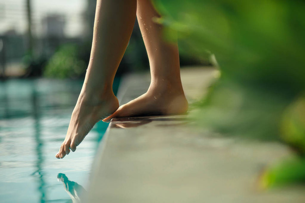 Closeup young female leg touch blue water in swimming pool - Photo, image