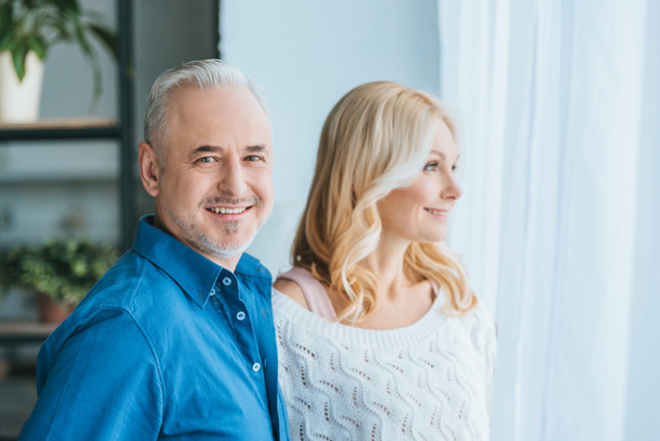 cheerful couple smiling while standing at home - Foto, Imagen