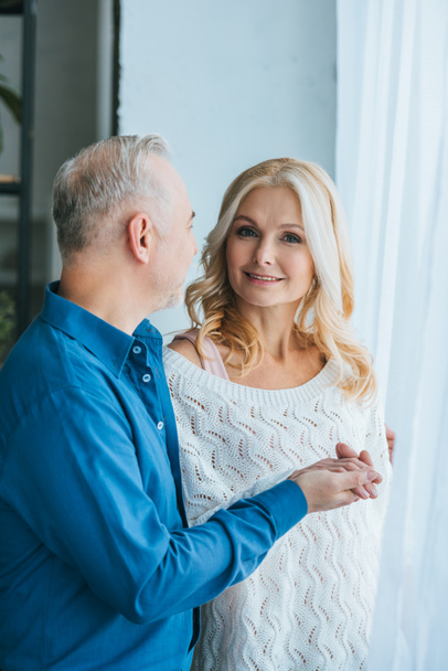 man looking at smiling wife while holding hands at home - Foto, Bild