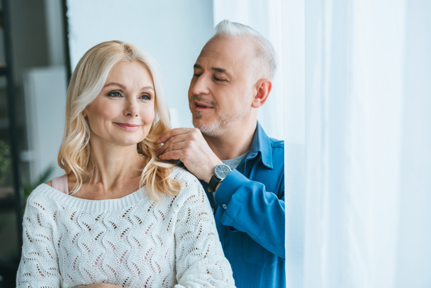 wesoły człowiek ogląda blond włosy uśmiechający się żona w domu - Zdjęcie, obraz
