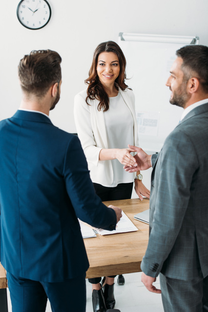 enfoque selectivo de asesor atractivo y sonriente e inversor estrechando la mano en el lugar de trabajo
  - Foto, imagen