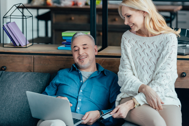 cheerful man looking at laptop near wife holding credit card - Foto, immagini