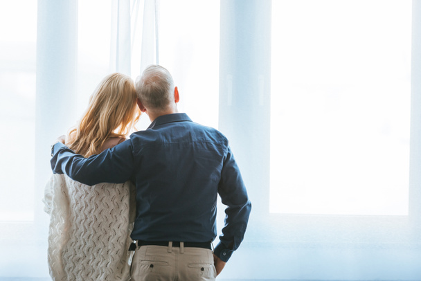 vista trasera de la pareja abrazándose cerca de la ventana en casa
 - Foto, Imagen