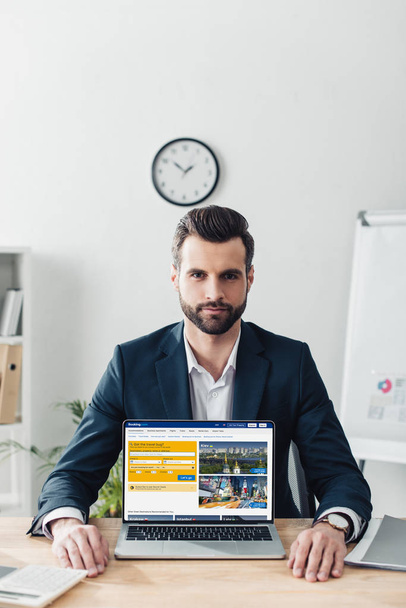 handsome advisor in suit showing laptop with booking website on screen  - Foto, immagini