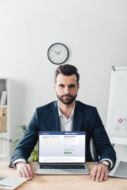 handsome advisor in suit showing laptop with facebook website on screen - Zdjęcie, obraz