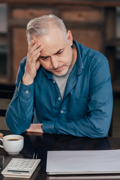 zmęczony człowiek trzyma głowę i patrząc na kubek z kawą - Zdjęcie, obraz