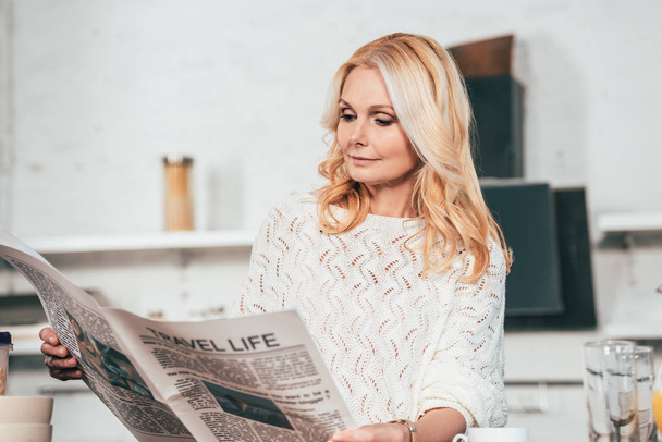 attractive blonde woman reading travel newspaper in kitchen  - Photo, Image