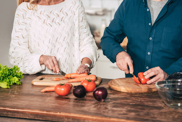 abgeschnittene Ansicht eines Paares beim Schneiden von Karotten und Tomaten in der Küche - Foto, Bild