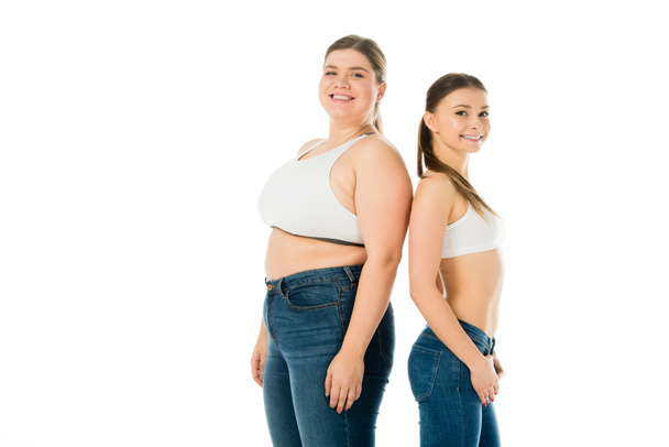 smiling slim and overweight women in denim posing together isolated on white, body positivity concept  - Photo, Image