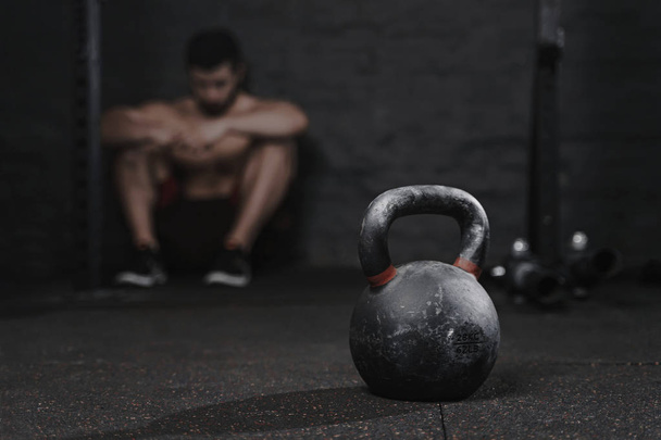 Sporty man sitting at the gym suffering breakdown to overcome. Demotivation sport concept. Stress and fatigue in sport. Crossfit kettlebell training. - Foto, afbeelding