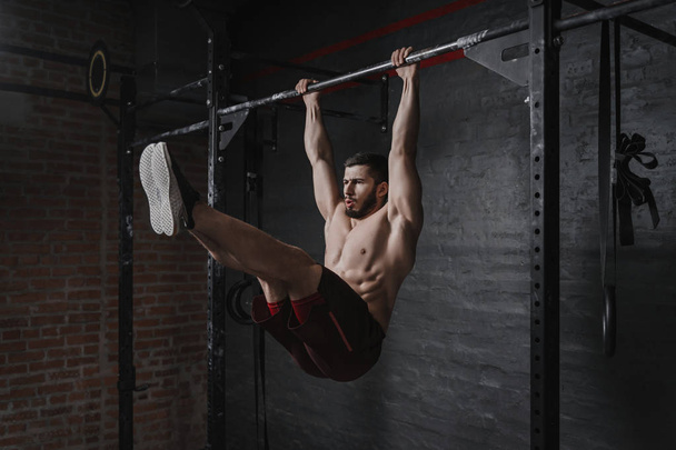 Atleta Crossfit haciendo ejercicios abdominales en barra horizontal. Practicar calistenia en el gimnasio
. - Foto, imagen