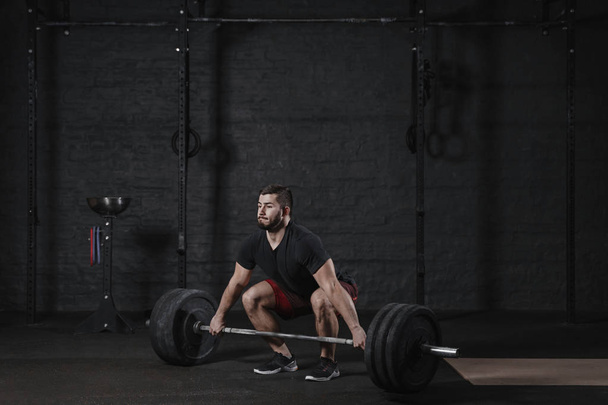 Young crossfit athlete doing deadlift exercise with heavy barbell at the gym. Man practicing functional training powerlifting workout - Foto, Imagen