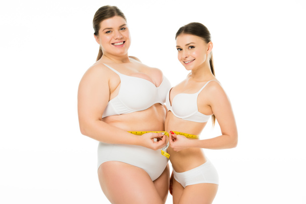 feliz cuerpo positivo mujer con sobrepeso y mujer delgada sosteniendo cinta métrica juntos aislado en blanco
 - Foto, Imagen