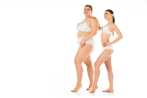 счастливые стройные и толстые женщины в нижнем белье позируют вместе изолированы на белом, концепция позитивности тела
 - Фото, изображение