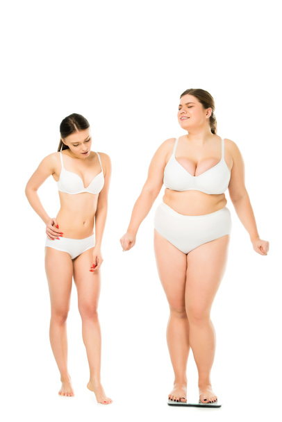 shocked slim woman in underwear looking at happy overweight woman on scales isolated on white, body positivity concept - 写真・画像