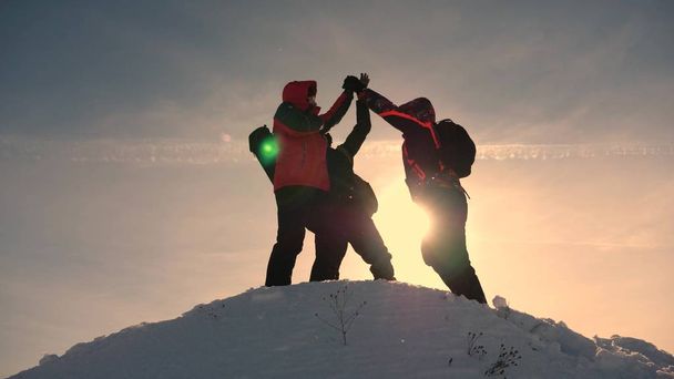 Teamarbeit und Sieg. Touristen kommen auf den verschneiten Hügel und freuen sich über den Sieg vor der Kulisse eines gelben Sonnenuntergangs. Teamarbeit von Menschen unter schwierigen Bedingungen. - Foto, Bild