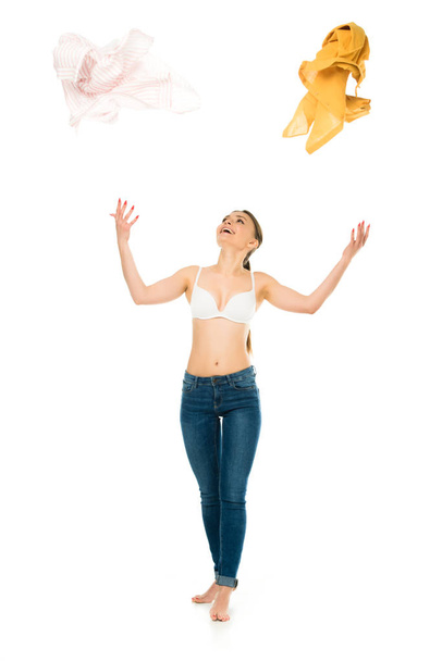 slim woman in underwear and blue jeans throwing up and looking at clothing isolated on white - Photo, Image