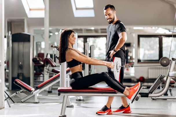 Pretty slim girl is doing exercises for the abdominals  on a special exercise machine under the supervision of a coach in the gym - Foto, Imagem