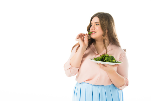 beautiful overweight woman eating fresh green spinach leaves from plate isolated on white - Фото, изображение