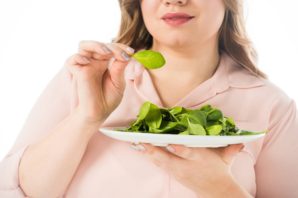 vista recortada de la mujer con sobrepeso comiendo hojas de espinacas verdes frescas de plato aislado en blanco
 - Foto, Imagen