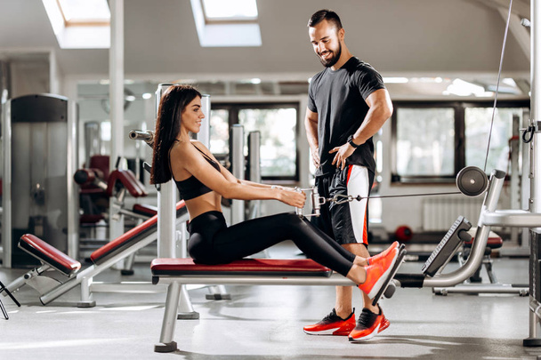 Pretty slim girl is doing exercises for the abdominals  on a special exercise machine under the supervision of a coach in the gym - Foto, imagen