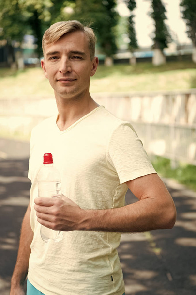 Thirsty man with water bottle on stadium. Sportsman with plastic bottle on sunny outdoor. Thirst and dehydration. Drinking water for health. Sport activity and energy - Zdjęcie, obraz