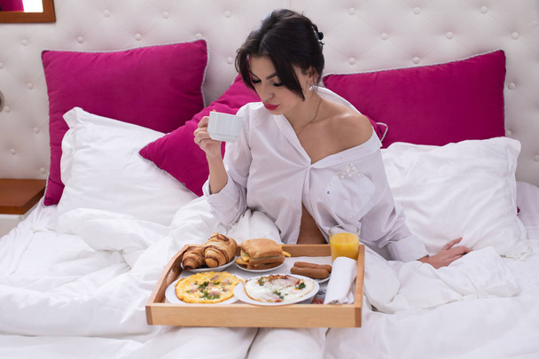 young woman in bed eating breakfast - Foto, afbeelding