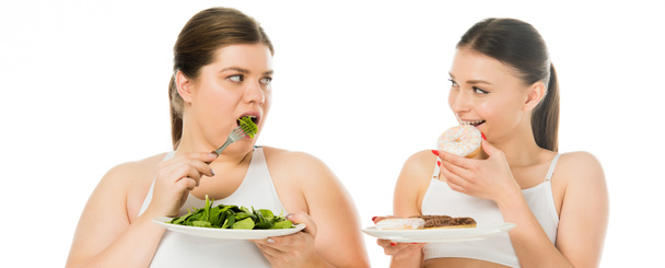 スリムな女性はドーナッツを食べと白で隔離緑のほうれん草の葉を食べて太りすぎの女性を見て - 写真・画像