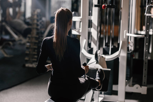 The beautiful athletic girl dressed dressed in a black sportswear is doing sport exercises with equipment on the bench in the modern gym - Фото, зображення