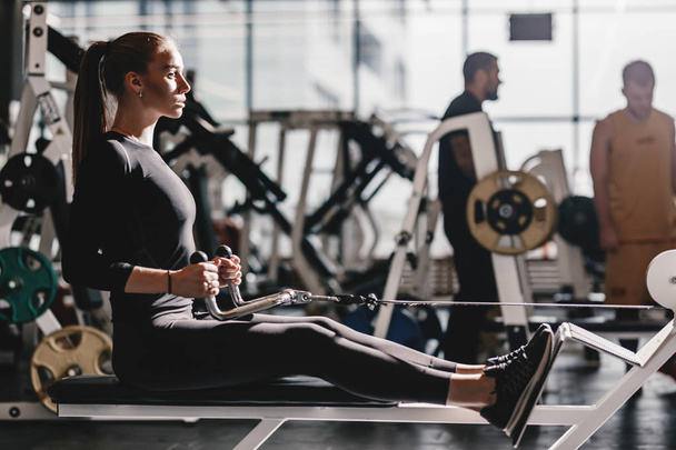 The beautiful athletic girl dressed dressed in a black sportswear is doing sport exercises with equipment on the bench in the modern gym - Foto, immagini